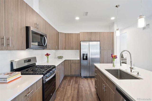 kitchen with hanging light fixtures, stainless steel appliances, backsplash, sink, and dark hardwood / wood-style flooring