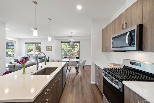 kitchen with backsplash, appliances with stainless steel finishes, dark hardwood / wood-style floors, decorative light fixtures, and sink