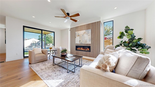 living room featuring a large fireplace, light hardwood / wood-style flooring, and ceiling fan