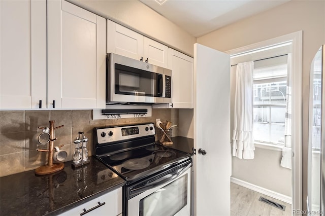 kitchen with stainless steel appliances, dark stone counters, decorative backsplash, light hardwood / wood-style floors, and white cabinetry