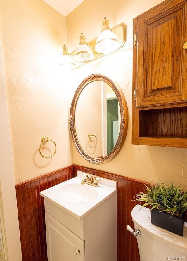 bathroom featuring vanity, wood walls, and toilet