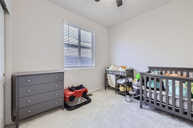 bedroom featuring light carpet, ceiling fan, a closet, and a crib