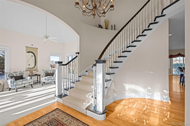 stairs featuring hardwood / wood-style flooring, a high ceiling, and ceiling fan with notable chandelier