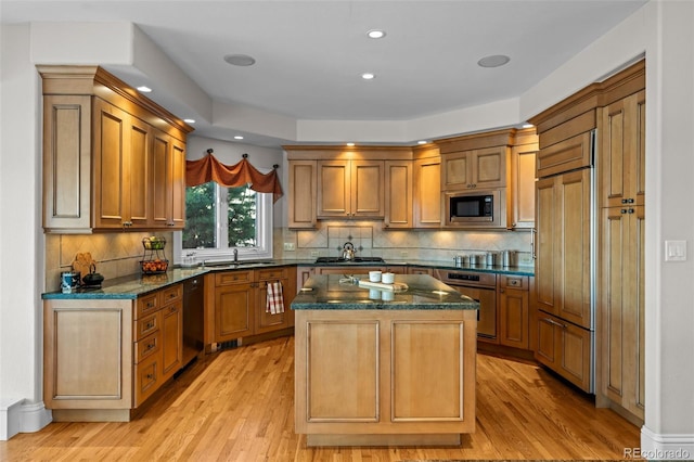 kitchen with dark stone countertops, a kitchen island, built in appliances, and light hardwood / wood-style flooring