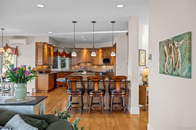 kitchen with stainless steel microwave, a wall mounted AC, backsplash, hanging light fixtures, and light hardwood / wood-style floors