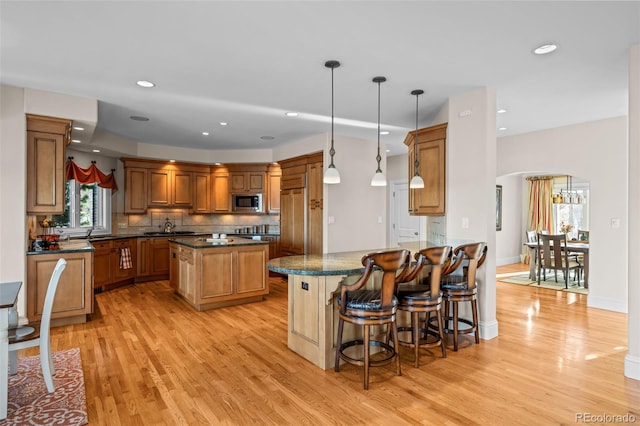 kitchen featuring built in appliances, decorative light fixtures, light hardwood / wood-style flooring, dark stone countertops, and decorative backsplash