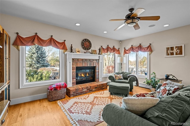 living room with a brick fireplace, hardwood / wood-style flooring, a baseboard radiator, and ceiling fan