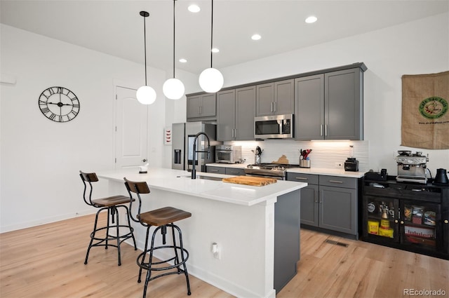 1929 W 165th Way, Broomfield, CO 80023 - kitchen featuring stainless steel appliances, gray cabinetry, a breakfast bar, light wood-style flooring, and a center island with sink