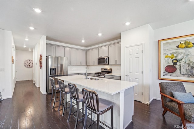 kitchen with dark hardwood / wood-style floors, a breakfast bar, gray cabinetry, appliances with stainless steel finishes, and a center island with sink