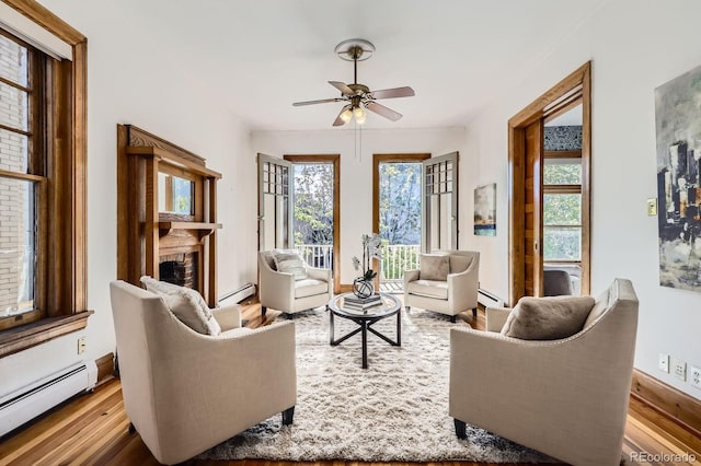 living area with a baseboard radiator, ceiling fan, wood finished floors, and a fireplace