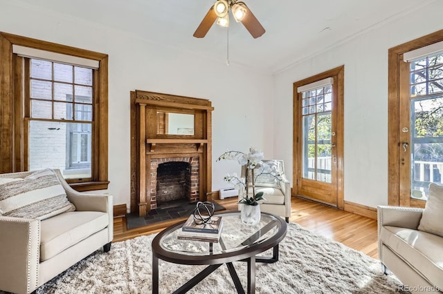 living area featuring baseboards, plenty of natural light, wood finished floors, a brick fireplace, and ornamental molding