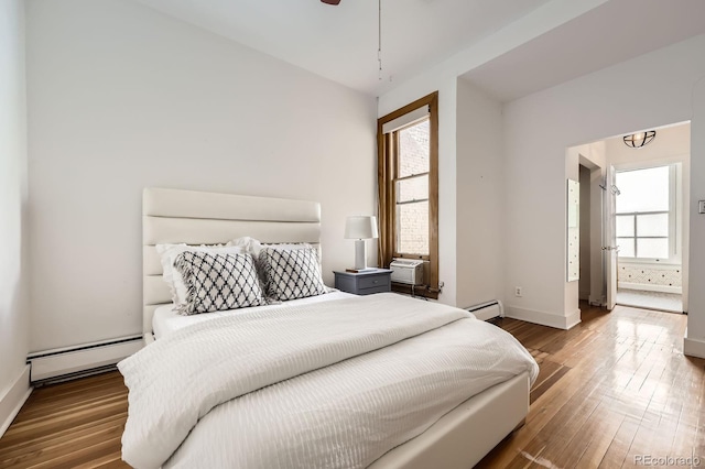 bedroom with a baseboard heating unit, wood finished floors, and baseboards