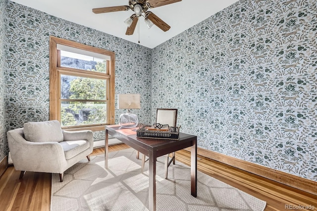 office space featuring wallpapered walls, wood finished floors, a ceiling fan, baseboard heating, and baseboards