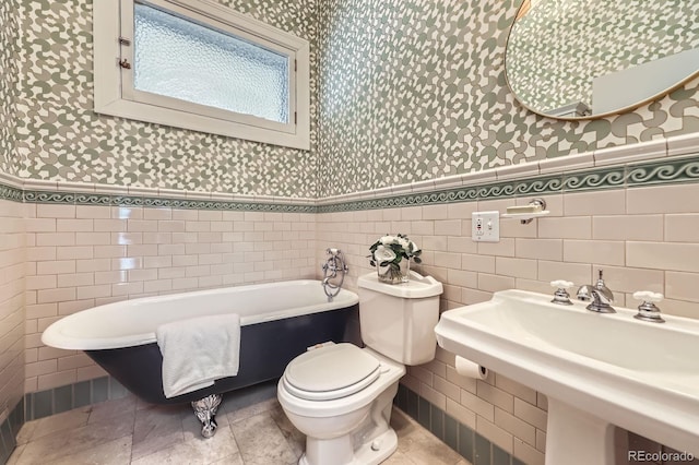 bathroom featuring wallpapered walls, tile walls, a soaking tub, toilet, and wainscoting
