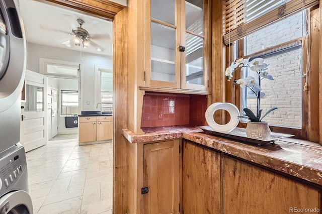 detailed view of stacked washer / dryer, ceiling fan, backsplash, and a sink