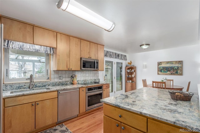 6905 Nelson St, Arvada, CO 80004 - kitchen featuring light stone countertops, light wood-type flooring, a sink, appliances with stainless steel finishes, and backsplash