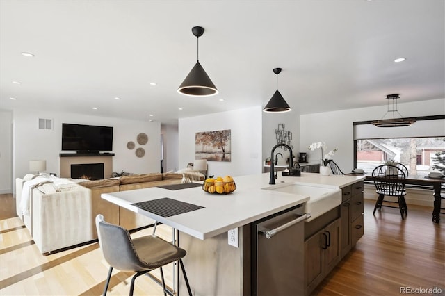 kitchen featuring sink, a kitchen island with sink, hanging light fixtures, stainless steel dishwasher, and light wood-type flooring