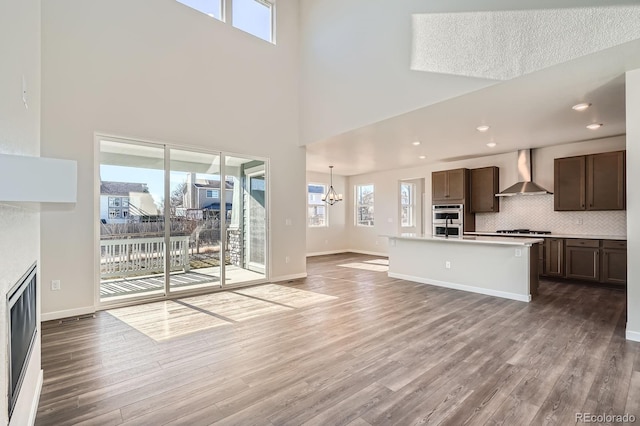 kitchen with wood finished floors, a notable chandelier, wall chimney exhaust hood, and open floor plan