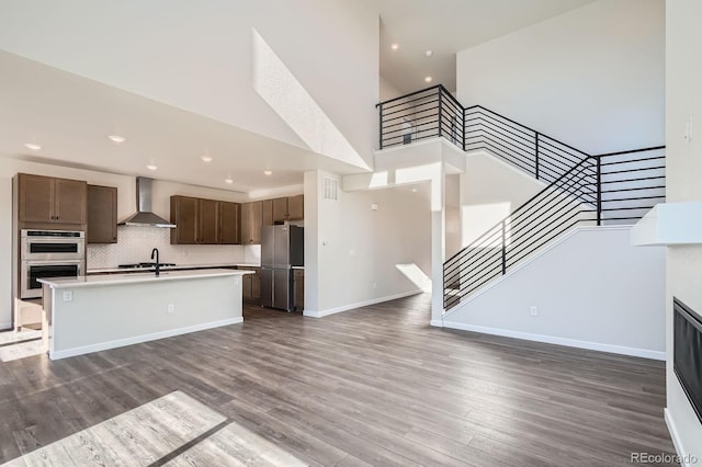 kitchen with wall chimney range hood, dark wood-style floors, open floor plan, and appliances with stainless steel finishes