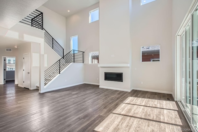 unfurnished living room with visible vents, a glass covered fireplace, stairway, baseboards, and dark wood-style flooring