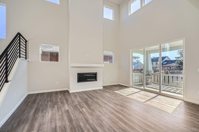 unfurnished living room featuring a glass covered fireplace, stairs, wood finished floors, and baseboards