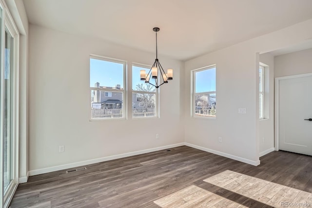 unfurnished dining area featuring wood finished floors, baseboards, a wealth of natural light, and a chandelier