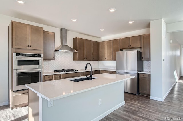 kitchen with wood finished floors, a sink, stainless steel appliances, light countertops, and wall chimney exhaust hood