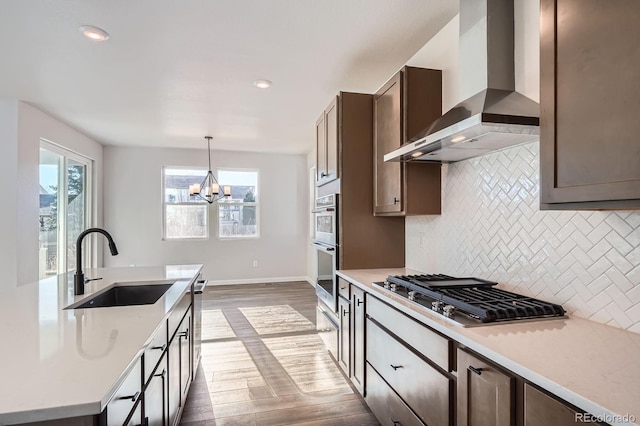 kitchen with light countertops, wall chimney exhaust hood, appliances with stainless steel finishes, and a sink