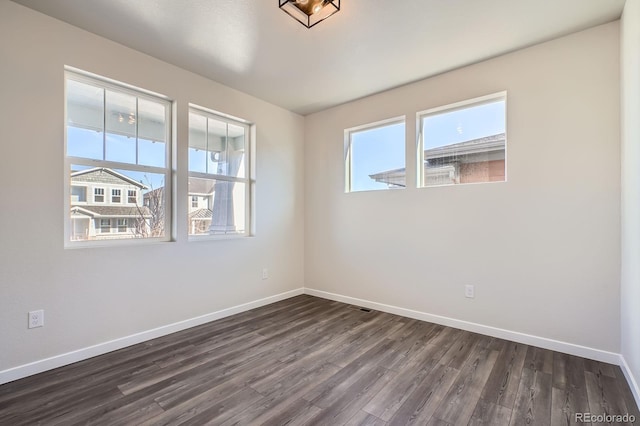 empty room with baseboards, plenty of natural light, and dark wood-style floors