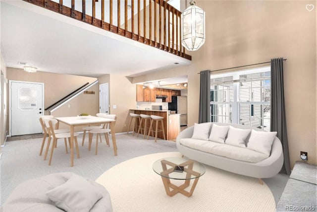 living area featuring a towering ceiling, an inviting chandelier, baseboards, and light colored carpet