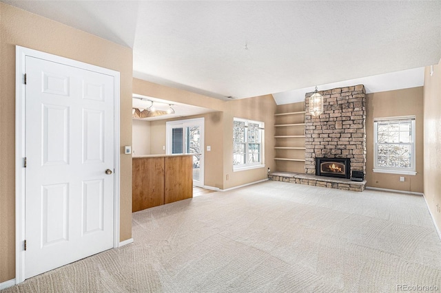 unfurnished living room with lofted ceiling, a textured ceiling, a stone fireplace, carpet flooring, and baseboards