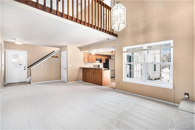 unfurnished living room with light carpet, baseboards, an inviting chandelier, stairs, and a high ceiling