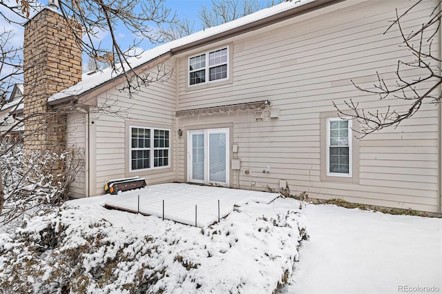 snow covered back of property with a garage and a chimney