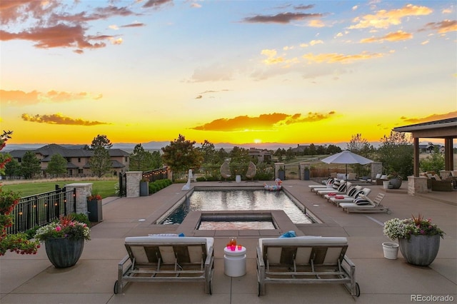 pool at dusk featuring a hot tub and a patio