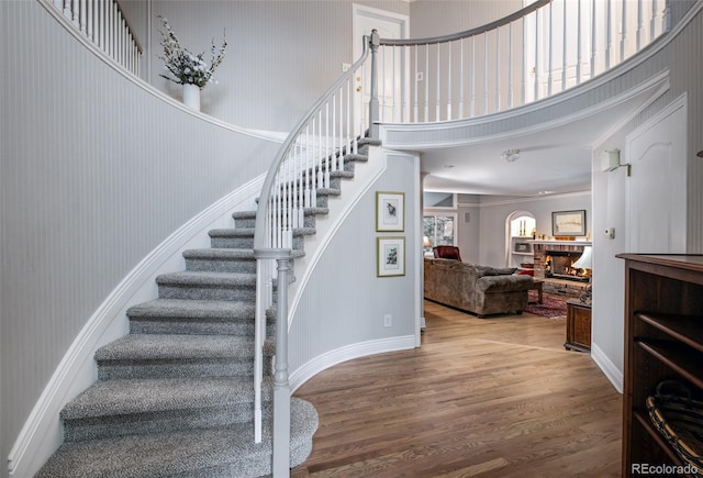 stairway with a high ceiling, hardwood / wood-style flooring, crown molding, and a fireplace