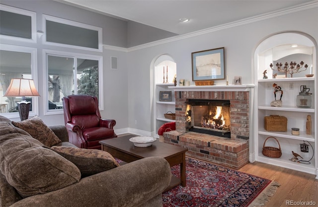 living room featuring a brick fireplace, ornamental molding, built in shelves, and light hardwood / wood-style flooring