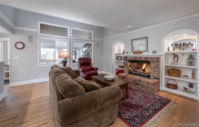 living room featuring a brick fireplace, built in features, light hardwood / wood-style floors, and crown molding