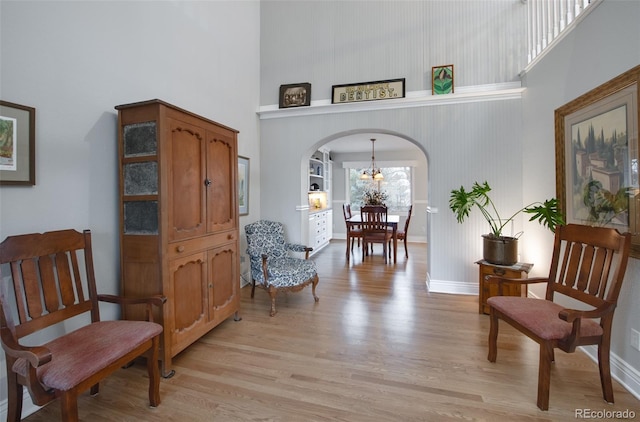 living area with a high ceiling, a chandelier, and light hardwood / wood-style floors