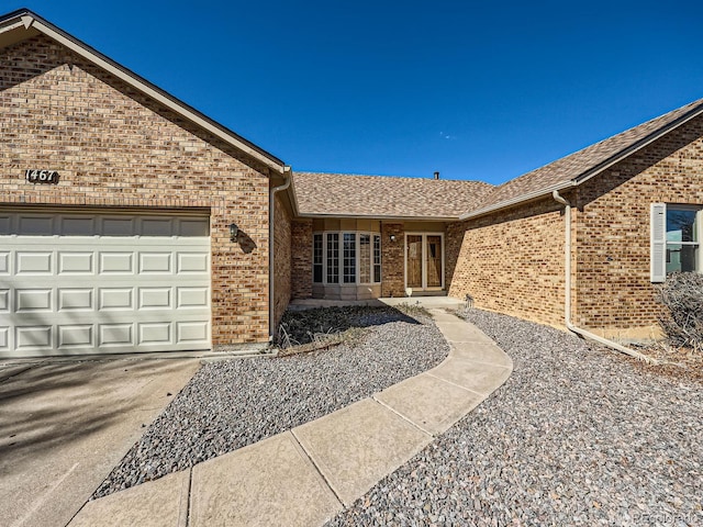 entrance to property with a shingled roof, brick siding, and an attached garage