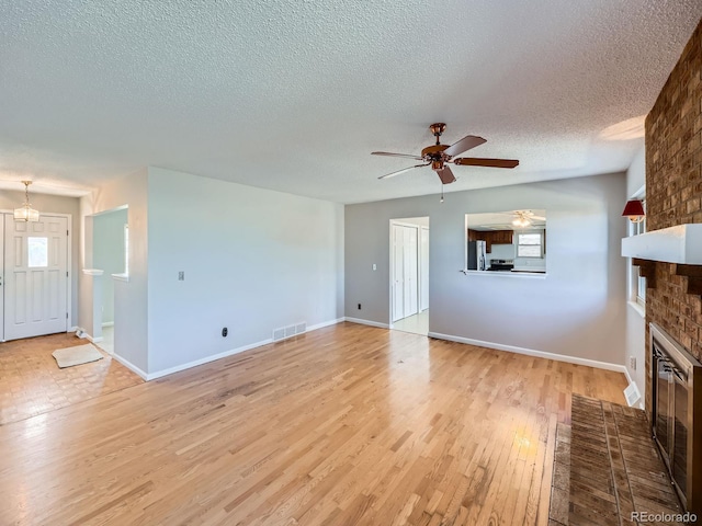 unfurnished living room featuring a textured ceiling, a fireplace, a ceiling fan, visible vents, and light wood-style floors