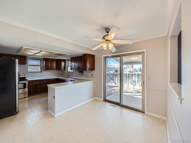 kitchen with dark brown cabinetry, a peninsula, stainless steel appliances, a textured ceiling, and light countertops