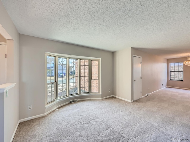 carpeted empty room with a textured ceiling, an inviting chandelier, visible vents, and baseboards