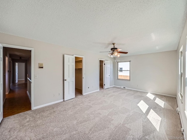 unfurnished bedroom with a textured ceiling, ceiling fan, light colored carpet, baseboards, and a walk in closet