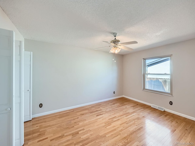 empty room featuring baseboards, visible vents, a textured ceiling, and light wood finished floors