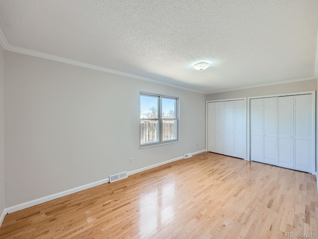 unfurnished bedroom with light wood-type flooring, visible vents, and multiple closets