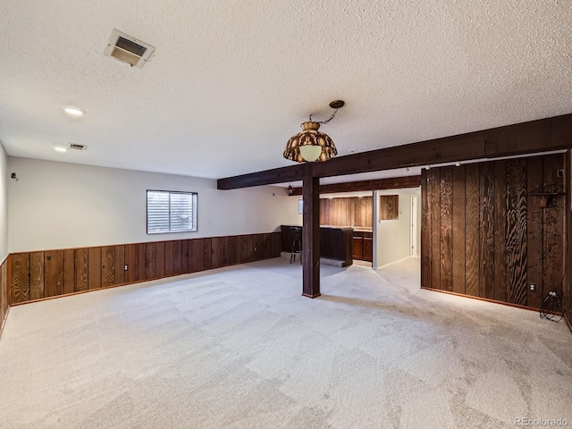 basement with wooden walls, visible vents, a wainscoted wall, a textured ceiling, and carpet floors