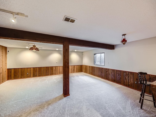 below grade area featuring a wainscoted wall, wood walls, a textured ceiling, and visible vents