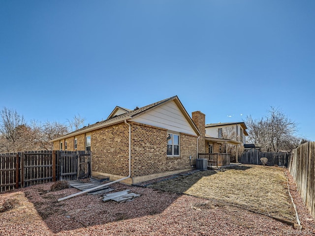 rear view of house featuring central AC, brick siding, a chimney, and a fenced backyard