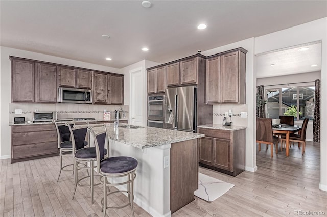 15647 Weaver Gulch Dr, Morrison, CO 80465 - kitchen featuring stainless steel appliances, light wood-style floors, light stone counters, a breakfast bar area, and recessed lighting