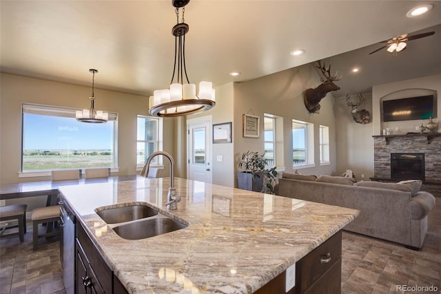 kitchen with pendant lighting, an island with sink, light stone countertops, and sink